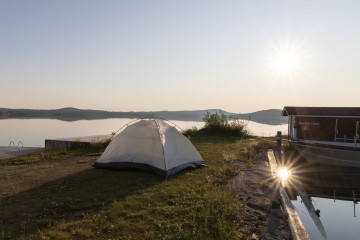 Nuoret nukkuu vaikka päällyskankaattomassa teltassa, lämpöisessä kesäyössä, aamu auringon noustessa, Inari järven rannalla